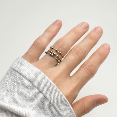 Hand wearing a stack of gold rings on a plain background