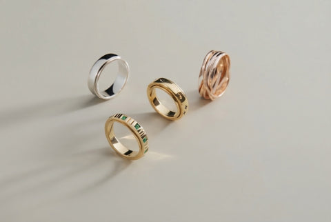 Group of four anxiety spinner rings, two gold, one silver, one rose gold, standing on their respective sides on a neutral light beige surface with offsetting shadows and reflection 