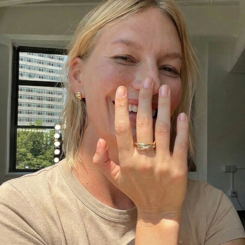 Person with a gold ring on their finger, indoors with a window in the background