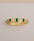 Gold ring with green gemstones on a light gray background