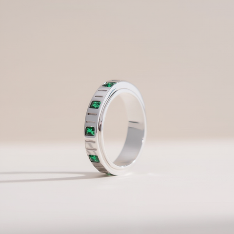 Silver ring with green gemstones on a light beige background