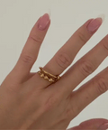 Hand wearing a gold ring with pink nail polish on a plain background