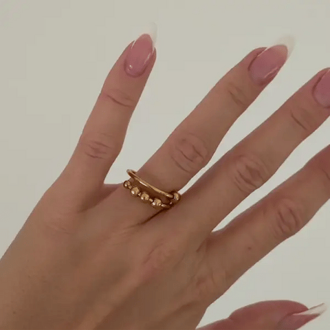 Hand wearing a gold ring with pink nail polish on a plain background