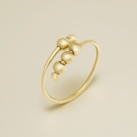 Gold ring with three spherical beads on a beige background