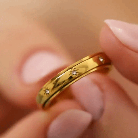 Macro shot GIF of two pairs of hands spinning a gold crystal eternity anxiety ring 