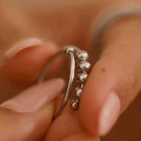 A macro shot of a hand holding a silver fidget ring, sliding the beads across the band. 