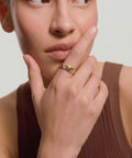 Woman wearing a gold ring on her finger, with a neutral background