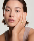 Woman wearing a gold ring on her finger against a neutral background