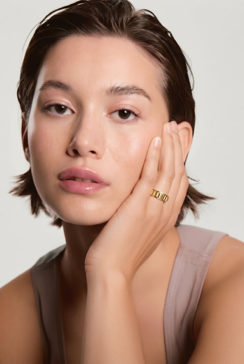 Woman wearing a gold ring on her finger against a neutral background