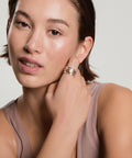 Woman wearing a multi-band silver ring on her finger, touching her neck, wearing a mauve tank top against a neutral background