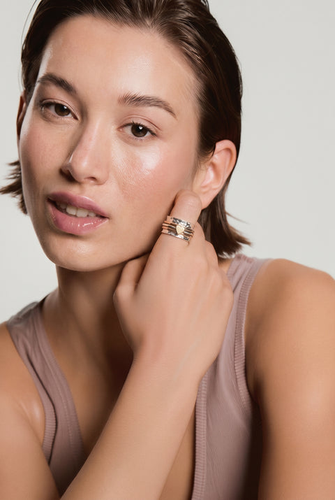 Woman wearing a multi-band silver ring on her finger, touching her neck, wearing a mauve tank top against a neutral background