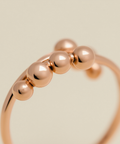 Rose gold ring with five beads on a beige background