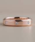 Rose gold ring with embedded diamonds on a neutral background
