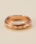 Rose gold ring with textured design on a beige background