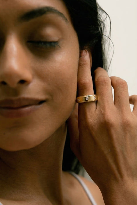 Woman holding her hand up to the side of her face, displaying a gold ring on her index finger 