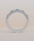 Silver ring with emeralds standing on its side with a beige neutral background. 