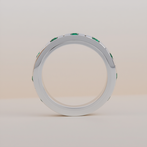 Silver ring with emeralds standing on its side with a beige neutral background. 