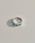 Silver ring with green gemstones on a light gray background