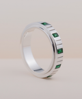 Silver ring with green gemstones on a light beige background