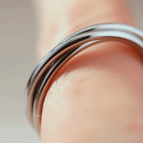 A macro shot of a hand gliding a Trinity silver fidget ring across their finger 