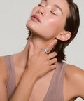 Woman with head tilted back and eyes closed, wearing a multi-band silver ring on her finger while touching her neck, in a mauve ribbed tank top