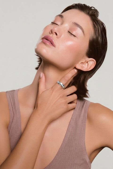 Woman with head tilted back and eyes closed, wearing a multi-band silver ring on her finger while touching her neck, in a mauve ribbed tank top