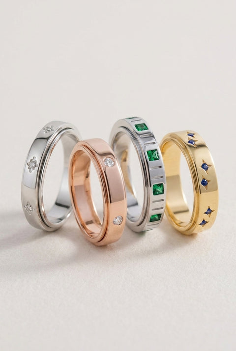 Four rings in silver, rose gold, and gold with gemstones on a light gray background