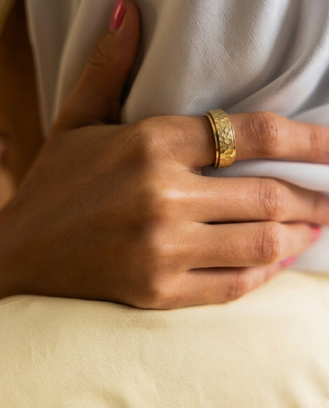 Close-up of a hand wearing a gold ring on a neutral background