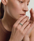 Close-up of a woman wearing a ring with green gemstones on a neutral background