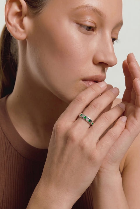 Close-up of a woman wearing a ring with green gemstones on a neutral background