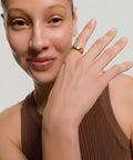 Woman wearing a gold ring on her finger against a neutral background