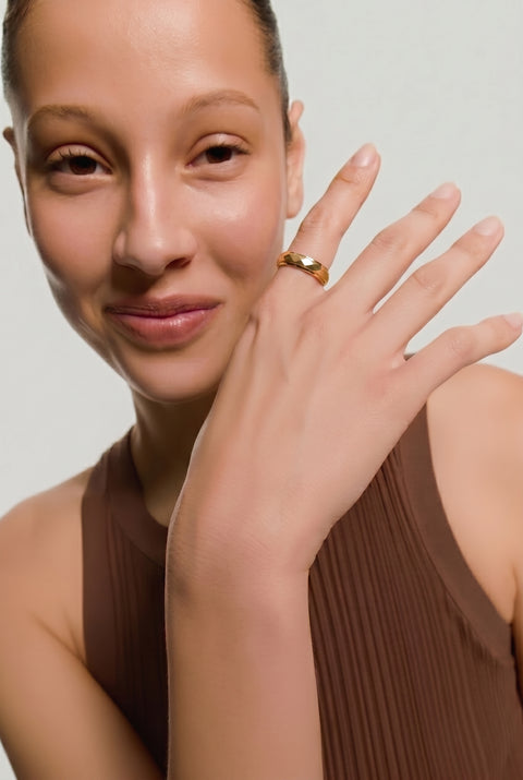 Woman wearing a gold ring on her finger against a neutral background