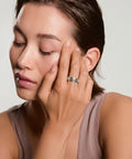 Woman with a ring on her finger touching her face against a neutral background