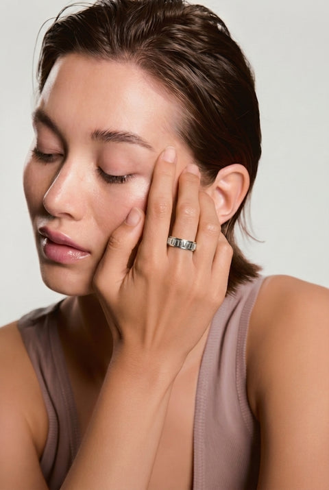 Woman with a ring on her finger touching her face against a neutral background