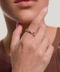 Close-up of a hand wearing a gold chain-link ring with a blue circular gemstone, touching the chin against a neutral background