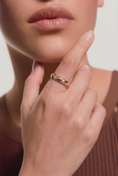 Close-up of a hand wearing a gold chain-link ring with a blue circular gemstone, touching the chin against a neutral background