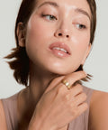 Woman with a gold ring on her finger against a neutral background