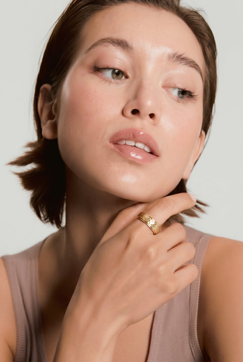 Woman with a gold ring on her finger against a neutral background