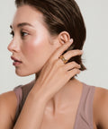 Woman adjusting a gold earring against a neutral background