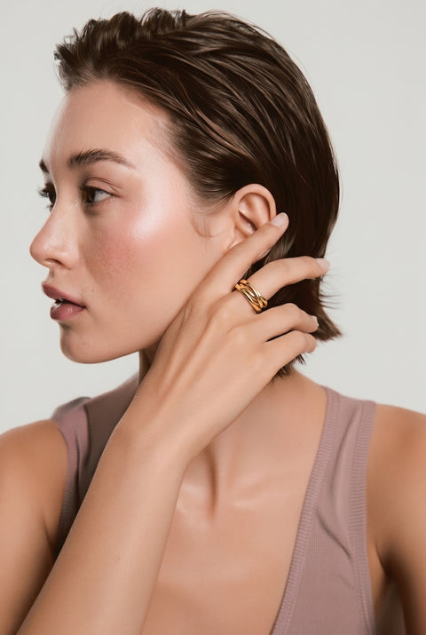 Woman adjusting a gold earring against a neutral background