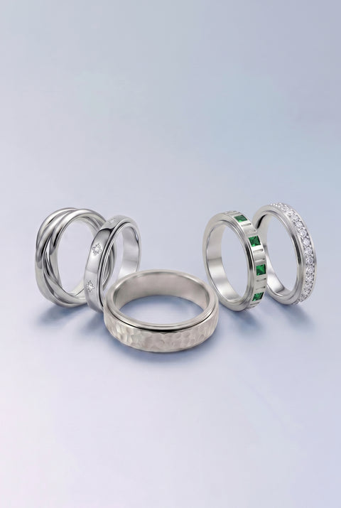 Four silver rings with different designs on a light gray background