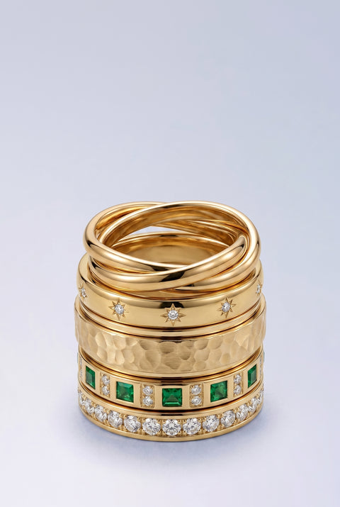 Stack of gold rings with gemstone accents on a light gray background