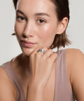 Woman with short dark hair resting her chin on her hand, showcasing a multi-band silver ring, wearing a mauve tank top against a light background
