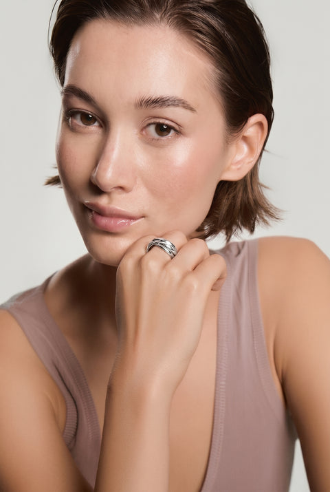 Woman with short dark hair resting her chin on her hand, showcasing a multi-band silver ring, wearing a mauve tank top against a light background