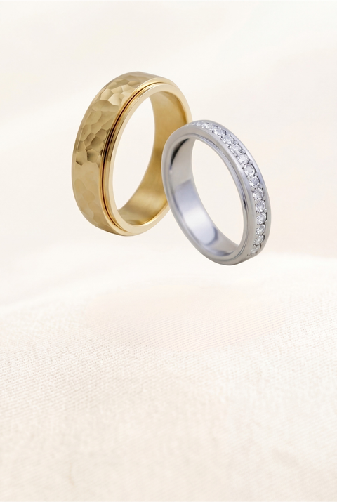 Two gold rings, one with a textured surface and the other with diamond accents, on a light background.